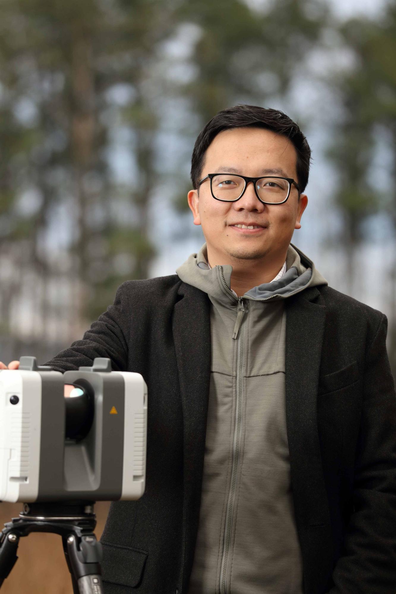 Photograph of Xi Yang. Photo of man in black coat and grey sweatshirt outdoors.